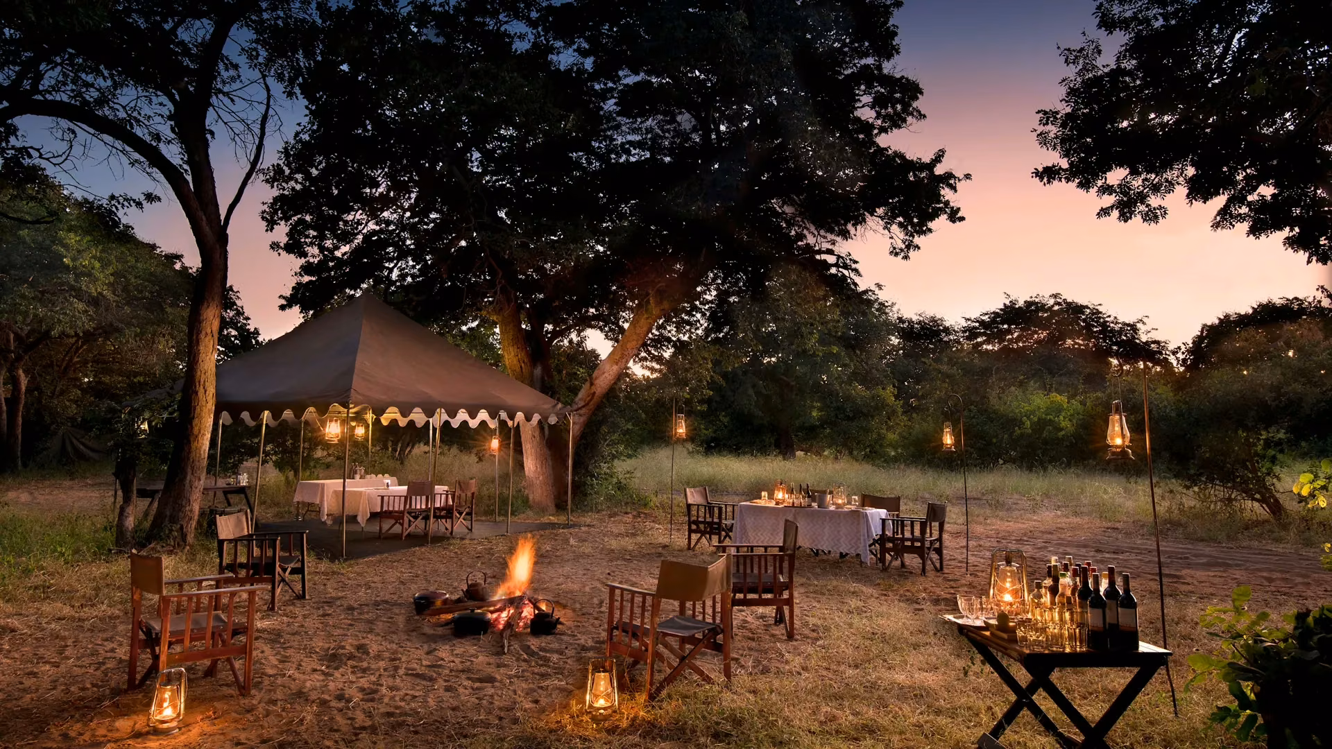 Campfire glowing beside the tents at dusk at Chobe Under Canvas