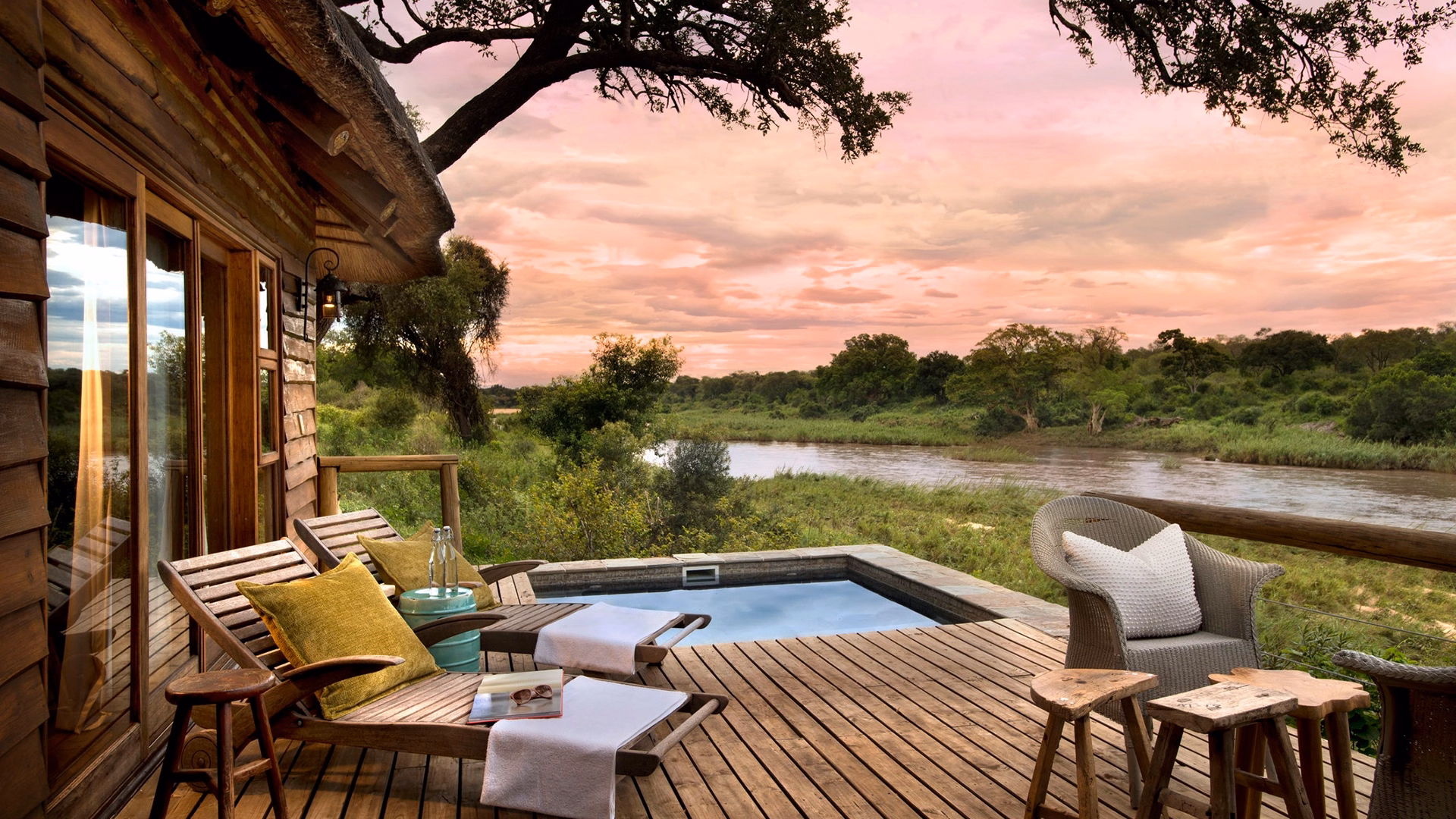Private suite deck at Narina Lodge, with a plunge pool and loungers overlooking the Sabie River and green bushveld under a pink sunset sky.