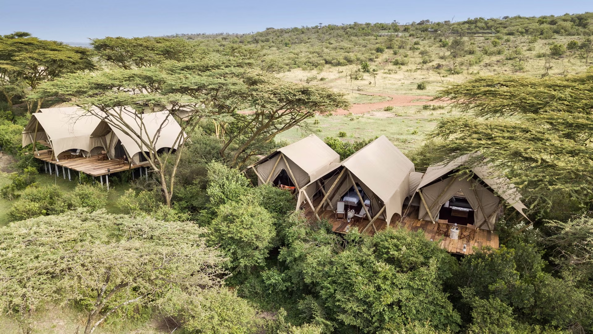 Aerial view of the canvas tented suites at Mara Nyika, raised on wooden decks among acacia trees and overlooking the open grasslands of the Maasai Mara, Kenya.